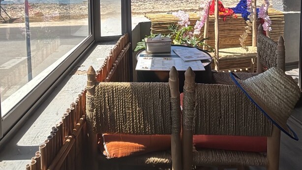 A room with a view of the beach, a table with a menu, and a hanging light fixture.