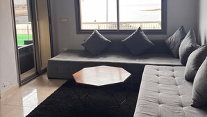 A modern living room with a sofa, a coffee table, and a large window offering a view of the sea.