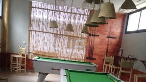 A pool table area with two tables, chairs, and hanging lamps.