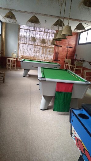 A pool table area with two tables, chairs, and hanging lamps.