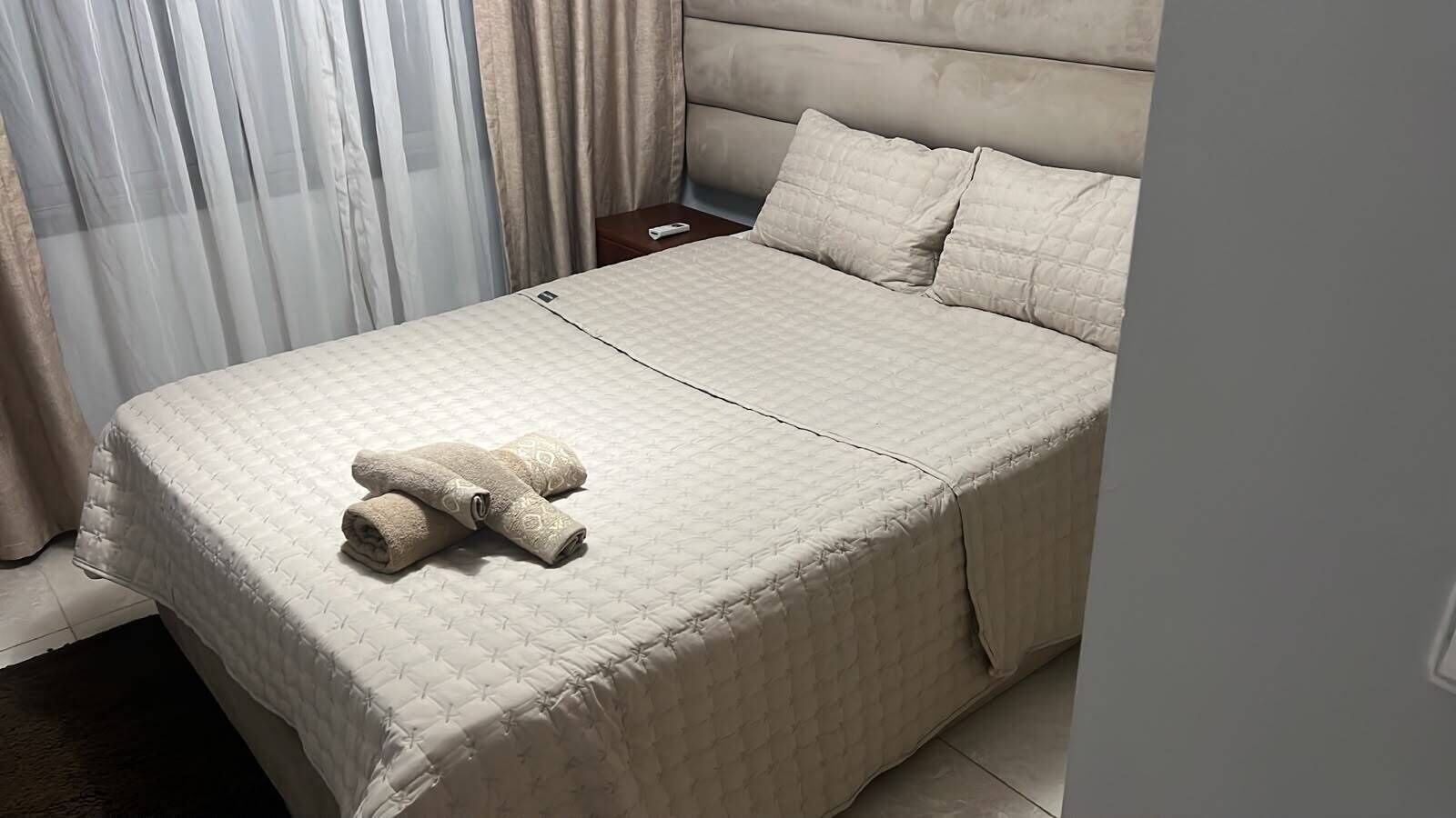 Una cama bien tendida con una colcha acolchada y dos toallas enrolladas.