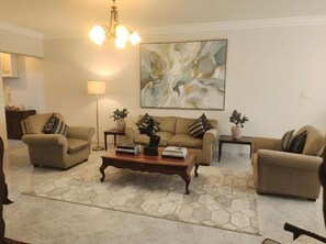 Una sala de estar con un conjunto de sofá, una mesa de centro con libros, una lámpara de pie y un cuadro abstracto grande en la pared.