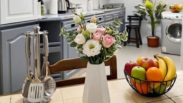 A kitchen with white cabinets, a vase with flowers, and a fruit bowl on the table. - Central luxury apartment 3 bedrooms (Cairo Governorate)