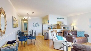 A compact living space with a dining area, a seating area with a sofa and armchairs, a kitchenette, and a sign indicating 'BEACH HOUSE'. - Reefs 7-3, Dog Friendly Beachfront Property, just steps away from the beach (Carolina Beach)