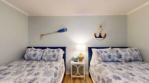 Ein Schlafzimmer mit zwei Betten, einem Nachttisch mit Lampe und Wanddekorationen, darunter ein Schläger und ein Anker.