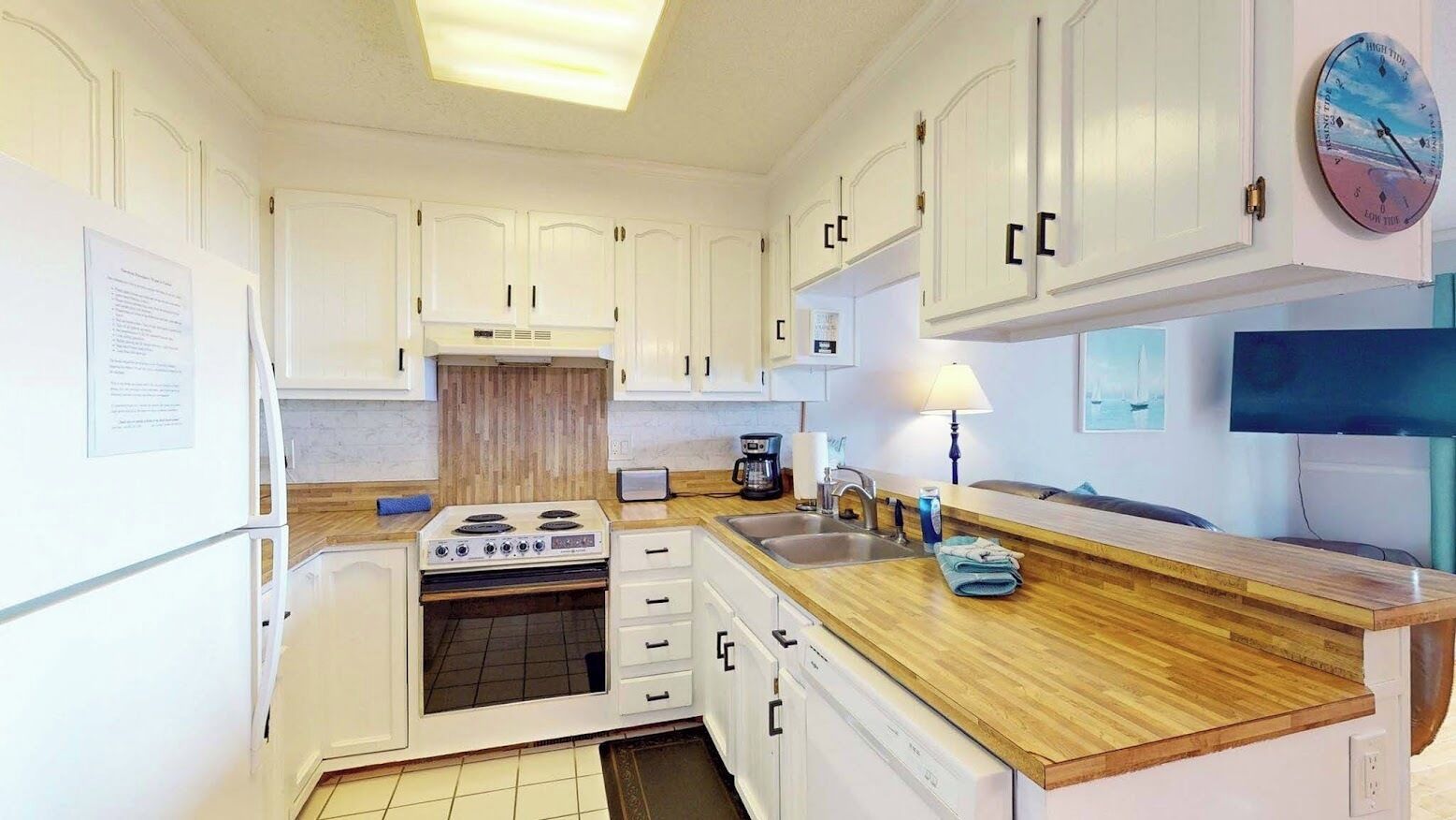 Une cuisine avec des meubles blancs, un plan de travail en bois, une cuisinière et un évier.