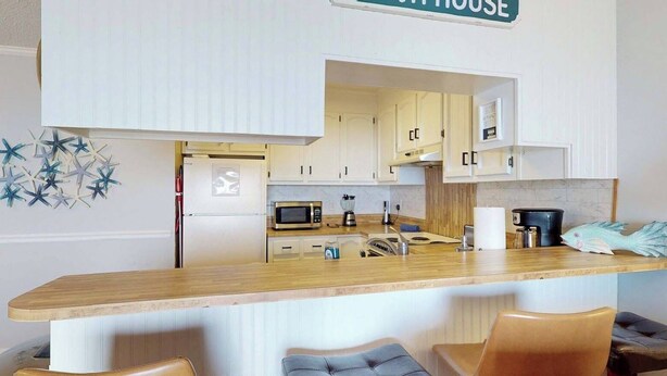A compact kitchen with white cabinets, a microwave, and a coffee maker. - Reefs 7-3, Dog Friendly Beachfront Property, just steps away from the beach (Carolina Beach)