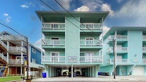 A multi-story building with balconies, a covered parking area, and a sign indicating 'Reefs Village.' - Reefs 7-3, Dog Friendly Beachfront Property, just steps away from the beach (Carolina Beach)