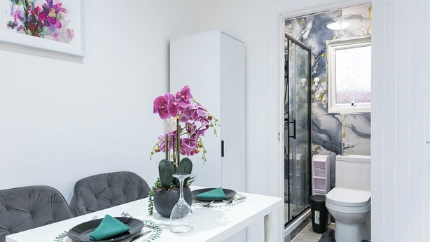 A dining area with a white table, grey chairs, a purple orchid, and a potted plant. - Studio Sleeps 2 With Parking (Thornton Heath)