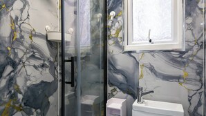 A bathroom with a glass shower enclosure, a white sink, and a marble-patterned wall. - Studio Sleeps 2 With Parking (Thornton Heath)