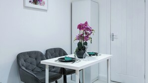 A dining area with a white table, two grey chairs, a potted orchid, and a cabinet. - Studio Sleeps 2 With Parking (Thornton Heath)