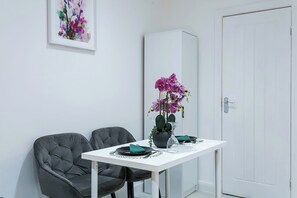A dining area with a white table, two grey chairs, a potted orchid, and a cabinet. - Studio Sleeps 2 With Parking (Thornton Heath)
