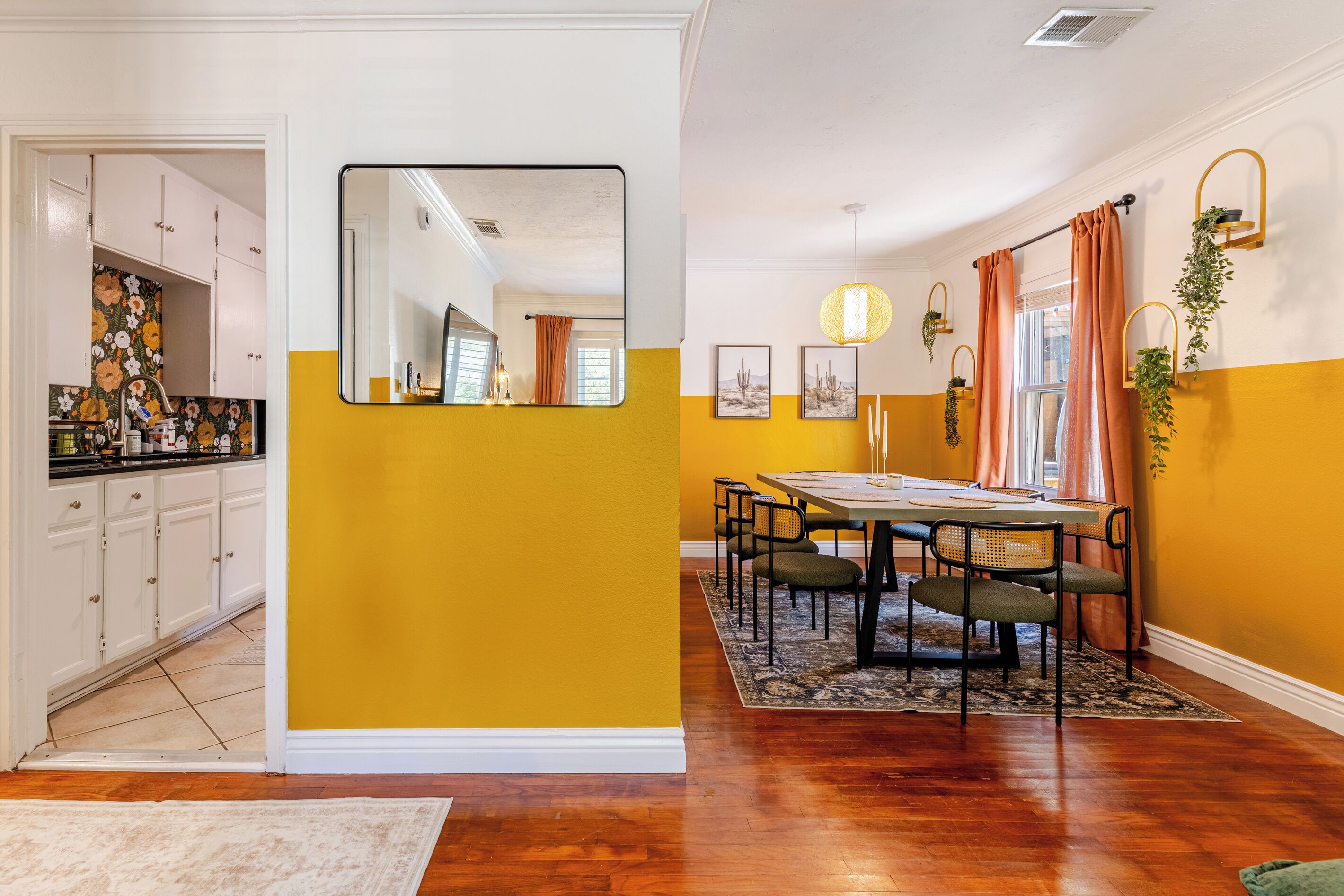Uma área de refeições com uma mesa posta para quatro pessoas, rodeada de cadeiras, e uma cozinha com armários e bancada visíveis ao fundo.