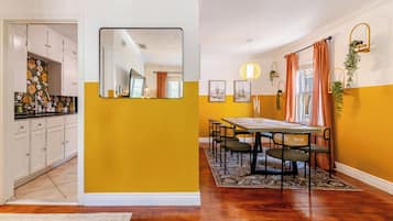 Uma área de refeições com uma mesa posta para quatro pessoas, rodeada de cadeiras, e uma cozinha com armários e bancada visíveis ao fundo.