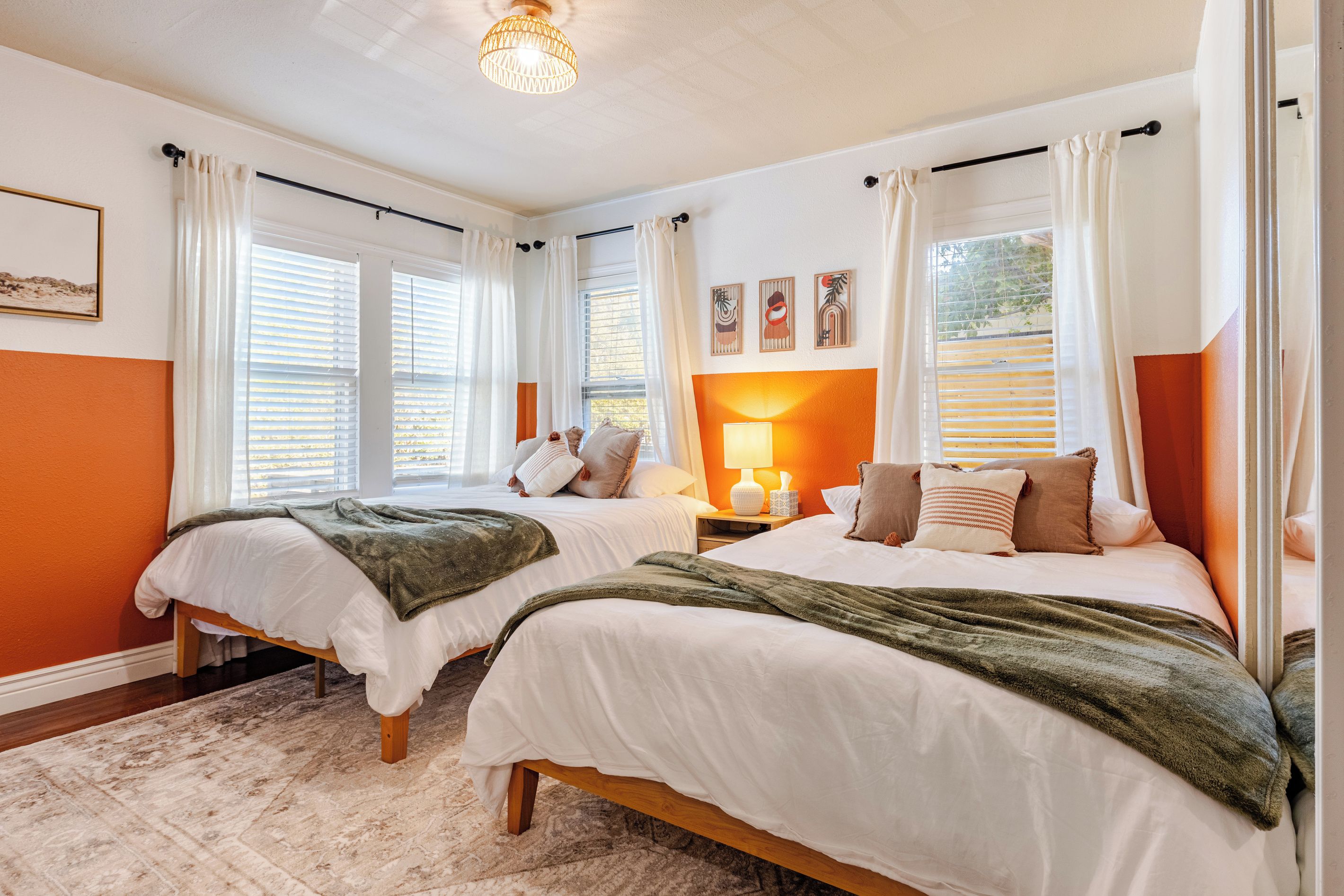 A bedroom with two beds, white bedding, a wooden floor, and a large window with curtains.