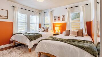 A bedroom with two beds, white bedding, a wooden floor, and a large window with curtains.