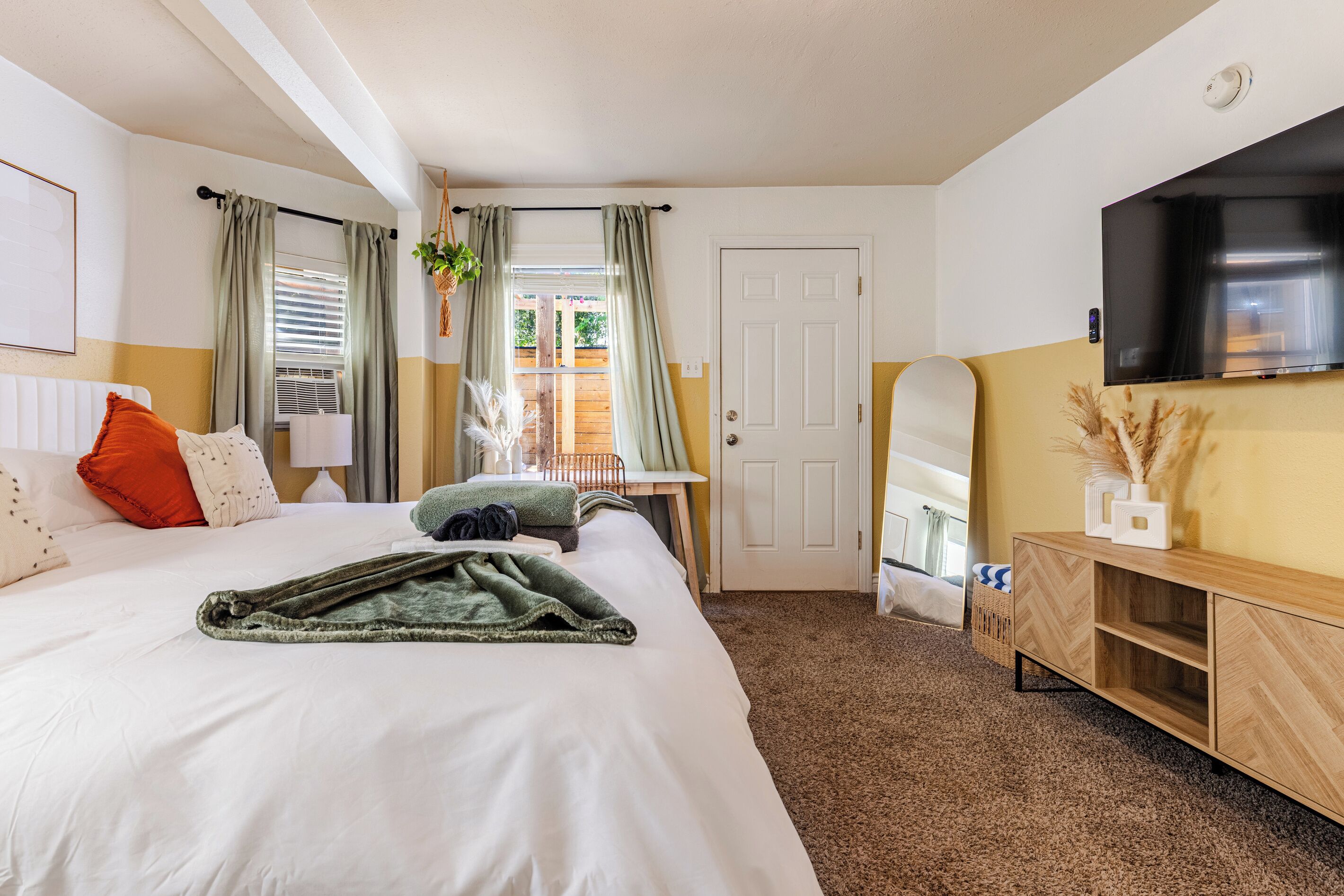 Quarto de hotel com cama, televisão, escrivaninha e porta.