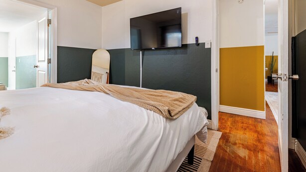 A hotel room with a bed, a television mounted on the wall, and a door leading to another room. - Tranquil Downtown Retreat w Private Pool & Hot Tub (Austin)