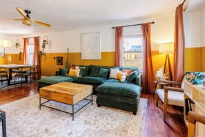 Ein Wohnzimmer mit einer Eckcouch, einem Holztisch und einem Essbereich mit Tisch und Stühlen.