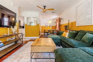 Ein Wohnzimmer mit Couchtisch aus Holz, grünem Sofa und Deckenventilator.