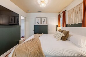 Ein Schlafzimmer mit einem Bett, einem Nachttisch, einer Lampe, einer Wanddekoration aus Makramee und gerahmten Kunstwerken.