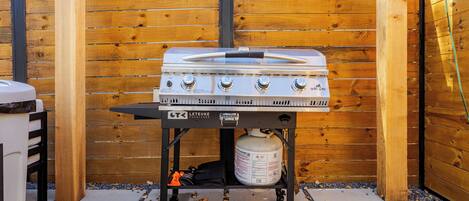 Un barbecue extérieur comprenant une bouteille de gaz, des boutons de réglage et un couteau posé sur le dessus.
