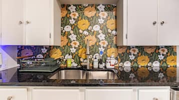Una cocina con salpicadero floral, pileta de acero inoxidable y armarios blancos.