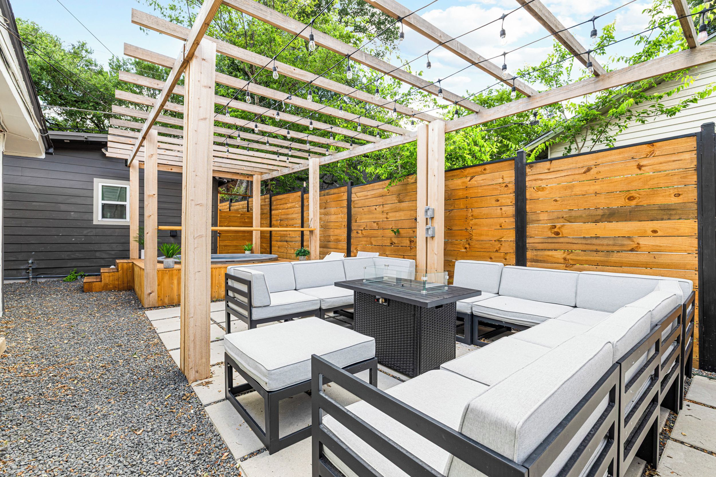 Ein überdachter Außenbereich mit Pergola, einem Tisch und einer Couch.
