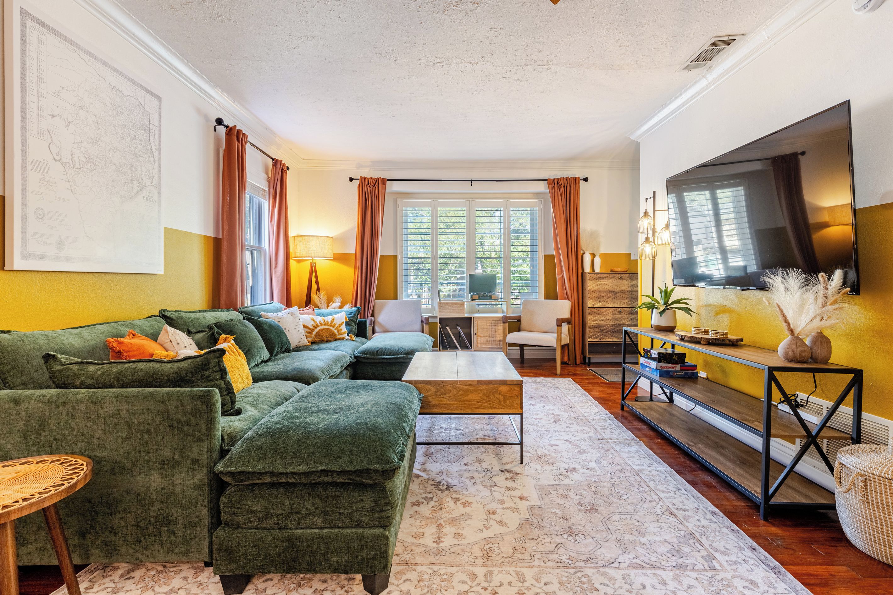 A living room with a sectional sofa, a coffee table, a TV, and a dining area with a table and chairs.
