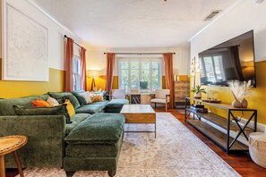 Ein Wohnzimmer mit Ecksofa, Couchtisch, Fernseher und einem Essbereich mit Tisch und Stühlen.