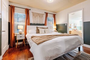 Een netjes ingerichte slaapkamer met een groot bed, nachtkastjes, een macramé wanddecoratie en uitzicht op een andere kamer.