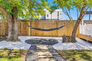 A hammock between trees, a fire pit, and a wooden fence in a backyard.