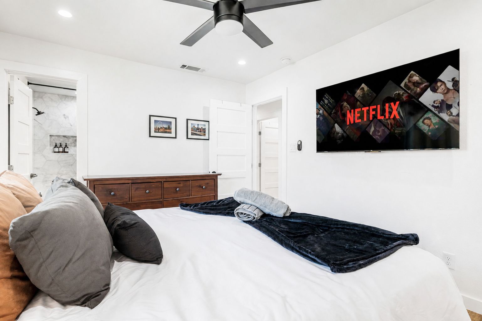 Un dormitorio con cama, almohadas, televisor montado en la pared y ventilador de techo.