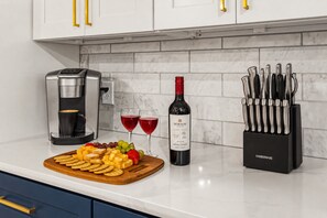 A kitchen with a coffee maker, wine bottle, glasses, fruit, and a knife block.