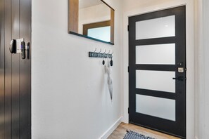 Una moderna entrata con una porta nera, un appendiabiti, uno specchio a parete e un dispositivo di sicurezza sulla porta.
