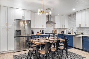 Una cucina moderna con mobili bianchi, un frigorifero in acciaio inossidabile, un tavolo da pranzo per quattro persone e un tappeto a motivi bianchi e neri.