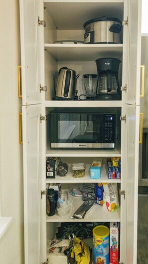 A kitchen pantry with a microwave, coffee maker, and various food items.