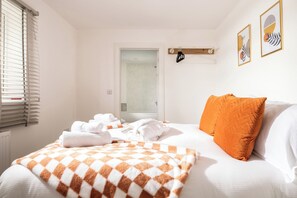 Ein Hotelzimmer mit einem Bett, einer karierten Decke, einem orangefarbenen Kopfkissen und einer sichtbaren Dusche hinter der Tür.