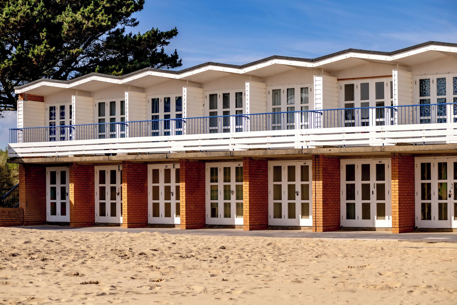 Um edifício à beira-mar com vários quartos, uma varanda e uma praia arenosa em primeiro plano.