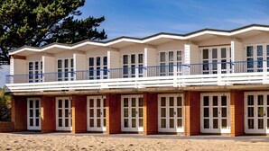 Un immeuble situé en bord de mer, doté de nombreuses pièces, d’un balcon et d’une plage de sable au premier plan.