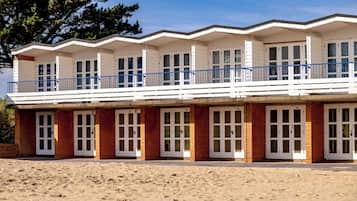 Um edifício à beira-mar com vários quartos, uma varanda e uma praia arenosa em primeiro plano.