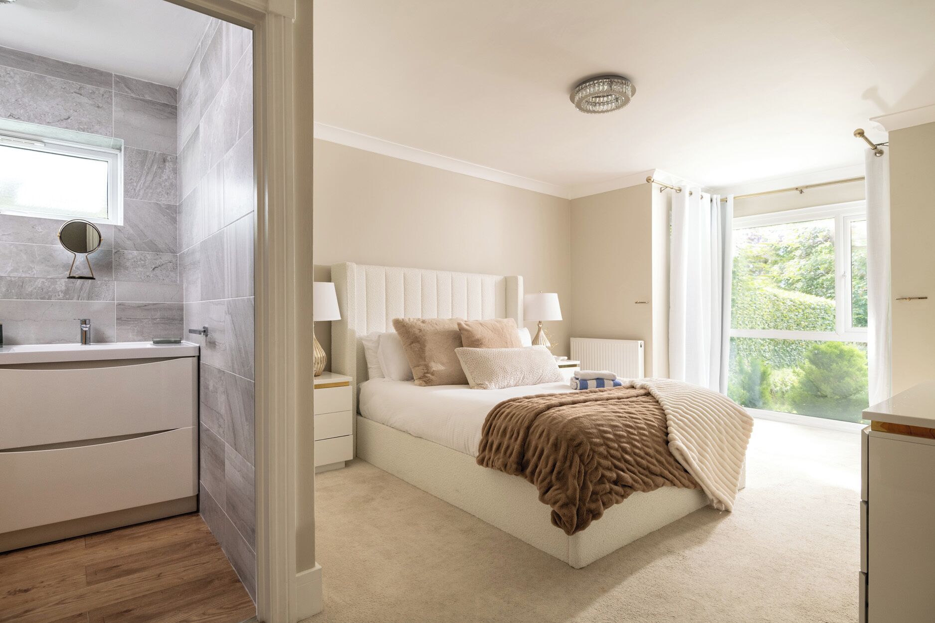 Quarto com uma cama grande, mesas de cabeceira, janela com cortinas e vista para o verde lá fora.