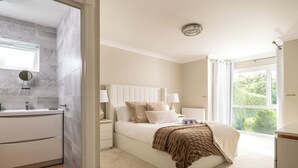 Une chambre avec un grand lit, des tables de chevet, une fenêtre avec des rideaux et une vue sur la verdure.