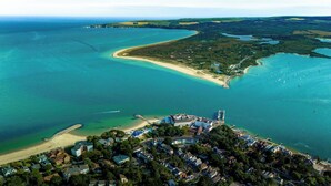 Une vue aérienne d’une zone côtière avec une plage, des eaux cristallines et un ensemble de bâtiments.