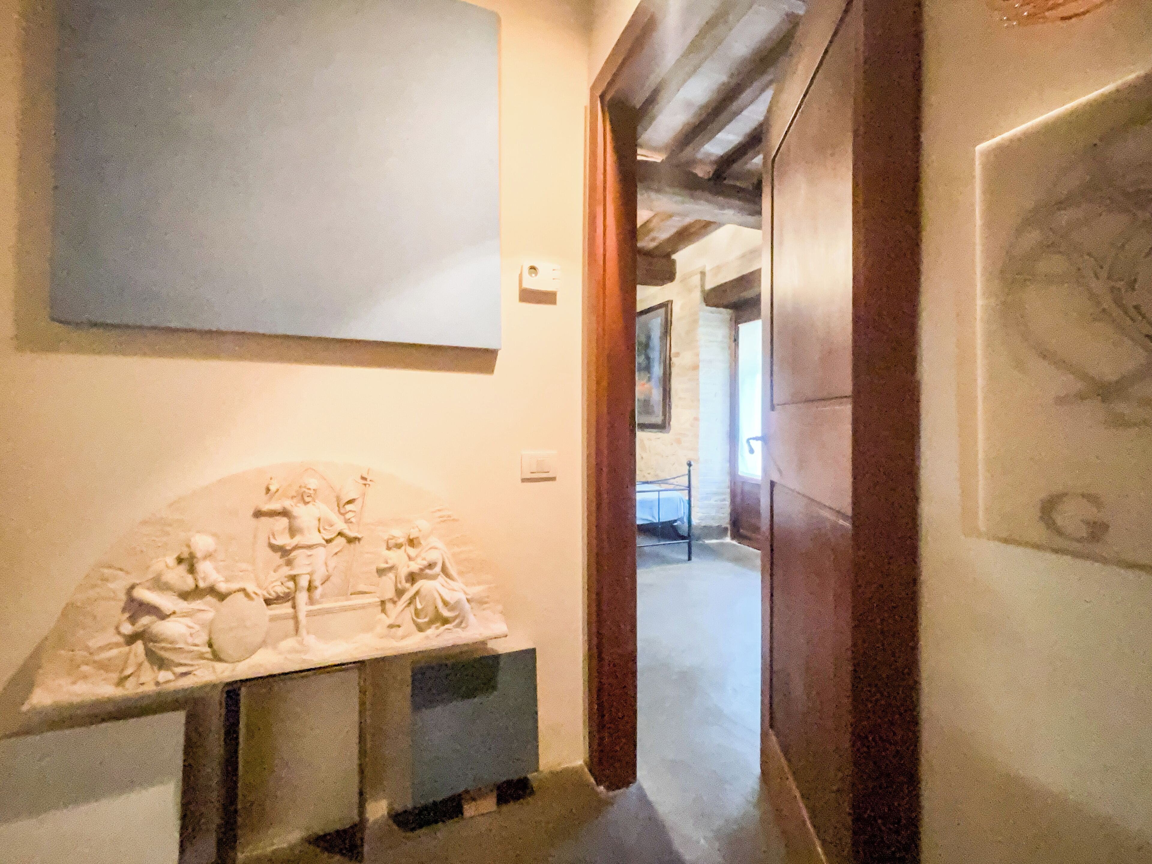 A hallway with a marble sculpture, a bed, and a door leading to another room.