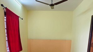 A room with a ceiling fan, two wooden chairs, a small table with a red cloth, and a red curtain. - Pet friendly cozy 1 BH for couples/families/groups (Coimbatore)