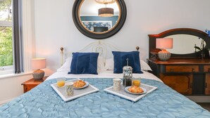 A neatly made bed with a blue quilt, a bedside table with a lamp, and a tray with breakfast items. - The Pines (Bournemouth)