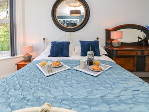 A neatly made bed with a blue quilt, a bedside table with a lamp, and a tray with breakfast items. - The Pines (Bournemouth)