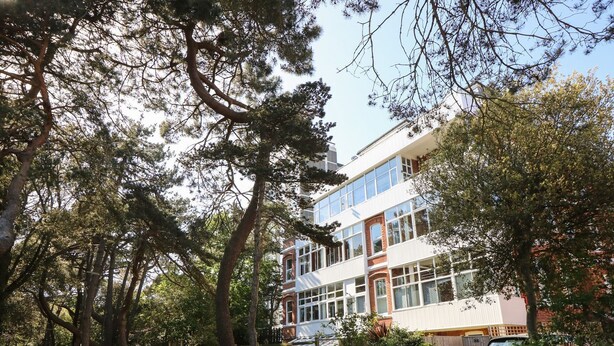 A multi-story building with large windows, surrounded by trees and a pathway. - The Pines (Bournemouth)