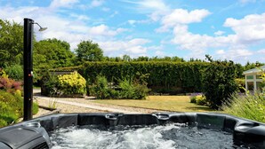 A hot tub in a garden with a clear sky and lush greenery. - Charming Countryside Cottage (Blandford Forum)
